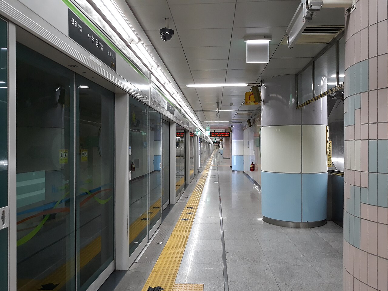 Empty subway platform with glass platform screen doors on the left, a yellow tactile strip and blue-and-white pillars