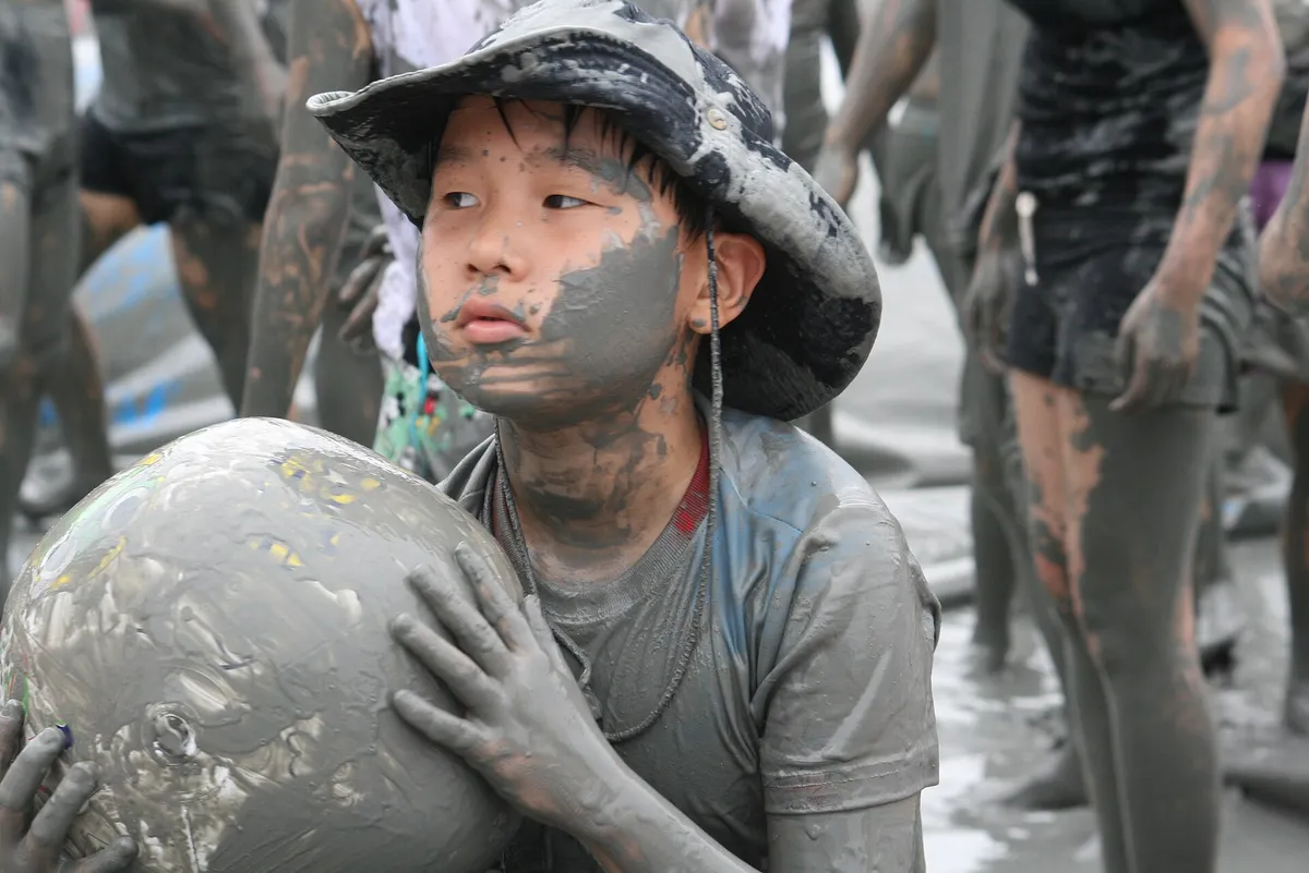 A child covered in grey mud holding a ball at the Boryeong Mud Festival
